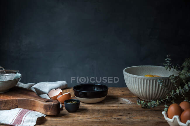 Bowl with eggs, flour and wooden spoon with pumpkin puree on wooden table during pastry preparation on dark background — Stock Photo