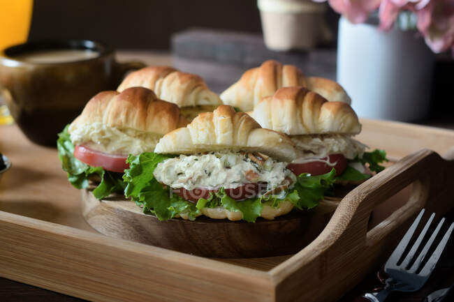 Deliciosos sanduíches de croissant com legumes servidos em bandeja com cappuccino e suco de laranja preparado para o café da manhã francês e colocado em mesa de madeira — Fotografia de Stock