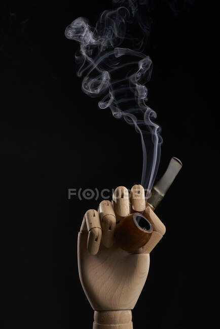 Traditional tobacco pipe with smoke in wooden hand on black background in studio — Stock Photo