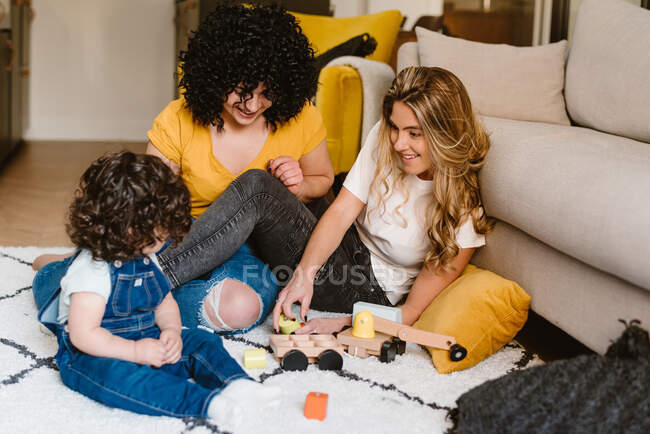 Full body content young lesbian couple in casual clothes playing with cute baby while sitting on floor in modern apartment — Stock Photo