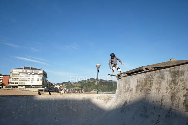 Unbekannter Teenager mit Schutzhelm fährt Skateboard in Skatepark an sonnigem Tag am Strand — Stockfoto