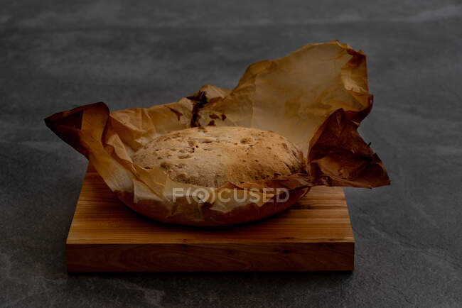 Pane rotondo artigianale appena sfornato con crosta croccante su carta pergamena posta su fondo nero — Foto stock
