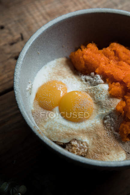 Ciotola con purea di zucca, uova e farina per la preparazione di torte sul tavolo di legno — Foto stock