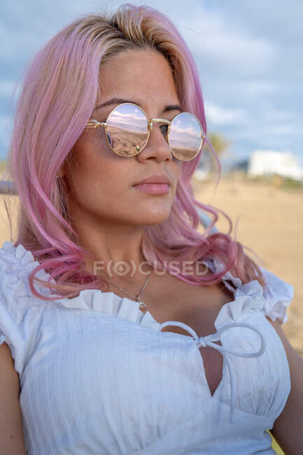 Relajada hembra con pelo rosa tumbada en tumbona y tomando el sol mientras se relaja en la playa durante las vacaciones de verano - foto de stock
