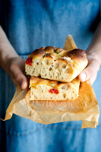 Crop person hands holding piece of fresh tomato focaccia with rosemary — Stock Photo