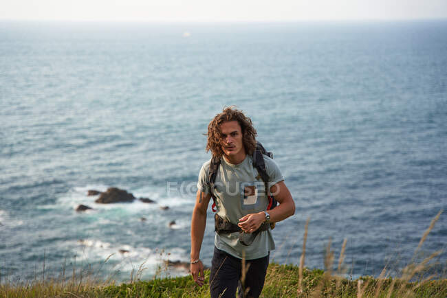 Чоловічий рюкзак, що ходить по пагорбу під час пішохідної подорожі влітку і дивиться на камеру — стокове фото