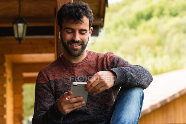 Zufriedene Männer hören Musik in Ohrhörern, während sie auf der Terrasse chillen und in den Pyrenäen ihr Smartphone benutzen — Stockfoto