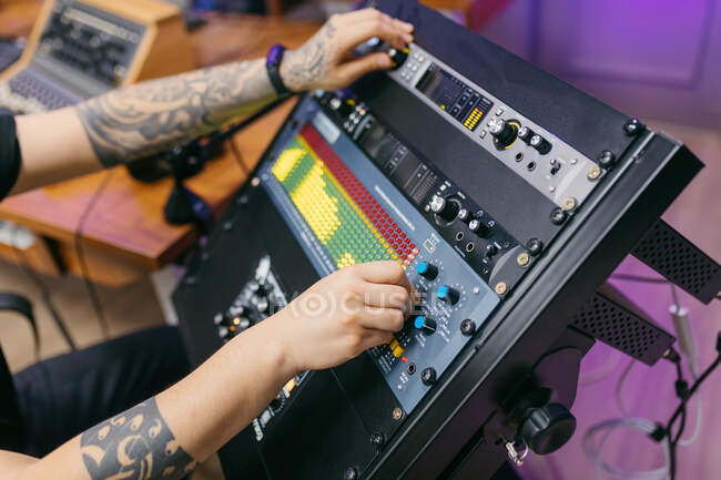 Vista lateral del cultivo irreconocible tatuado ingeniero de sonido masculino que trabaja con el panel de control en la placa de audio en el estudio de grabación - foto de stock