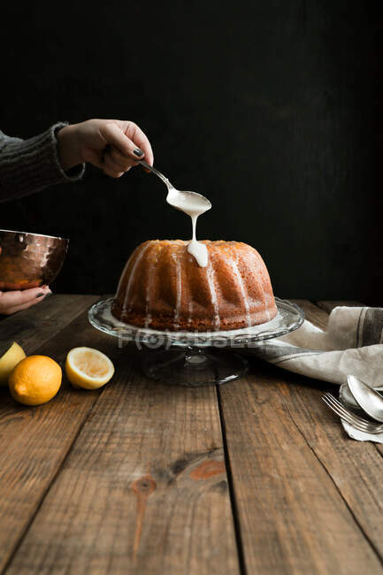 Vue de la récolte du revêtement à la main avec une cuillère un gâteau éponge citron placé sur une table en bois sur un fond sombre — Photo de stock