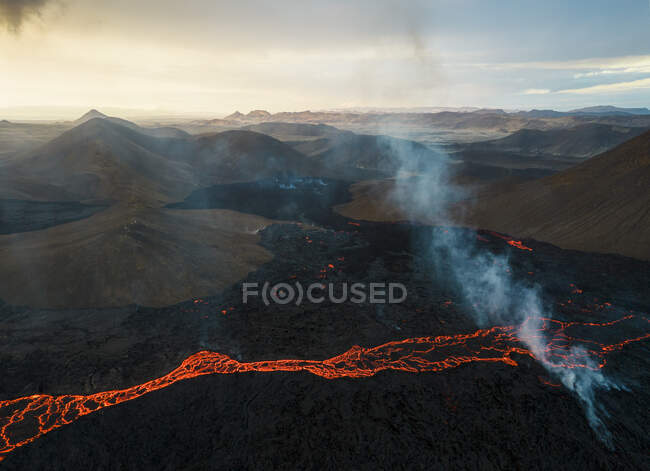 Drone vista del torrente di lava arancione calda che scorre attraverso terreni montuosi al mattino in Islanda — Foto stock
