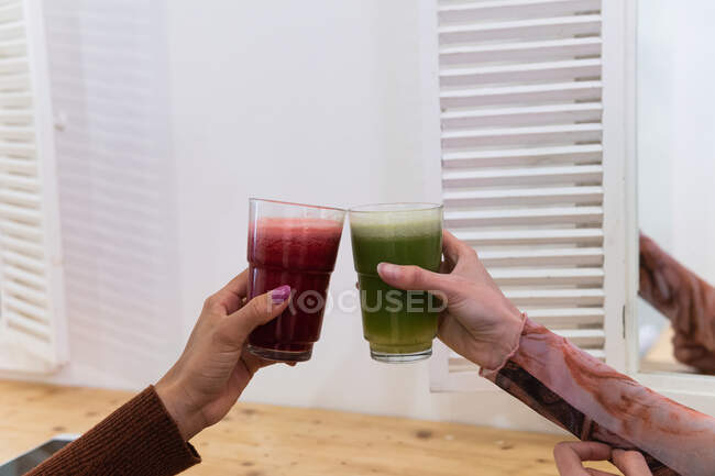 Cropped unrecognizable multiethnic female friends sitting at counter and drinking refreshing smoothie while chilling in bar — Stock Photo