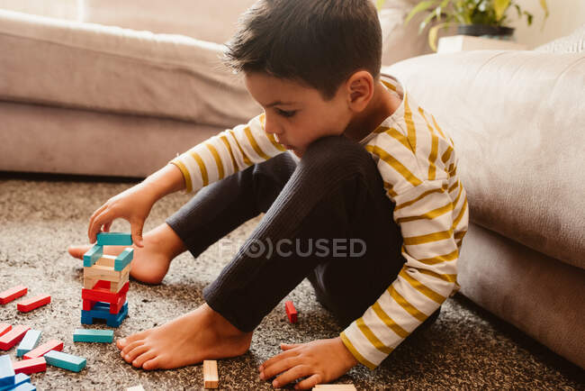Вид сбоку мальчика, играющего со стройматериалами в столовой дома — стоковое фото