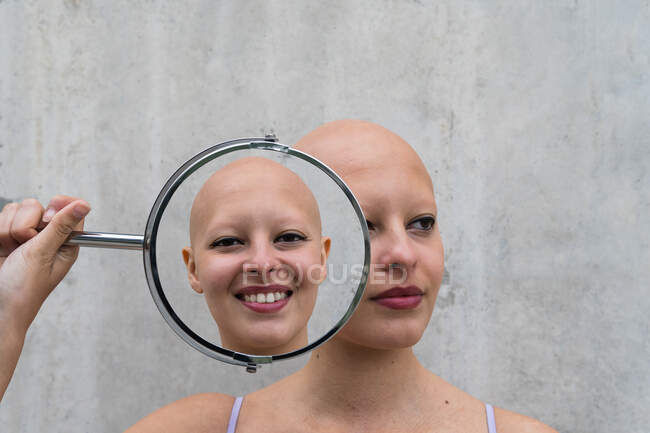 Doppelbelichtung junger kahlköpfiger Frauen mit Alopezie-Autoimmunerkrankung, die einen runden Spiegel in Gesichtsnähe halten, der unterschiedliche Reflexionen aufweist — Stockfoto