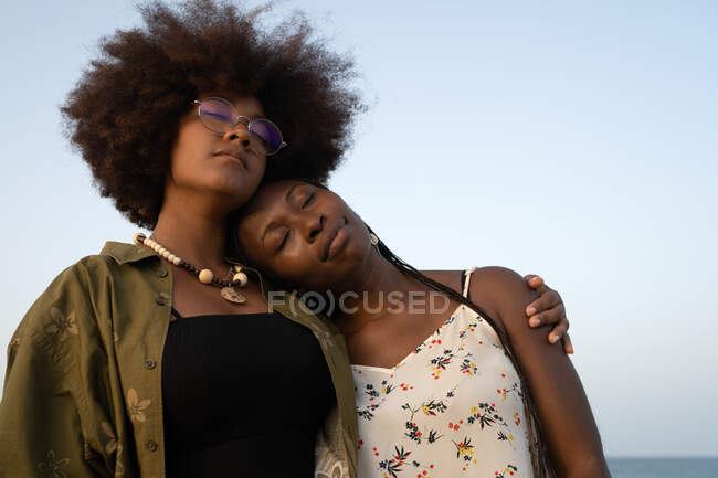 Счастливые молодые афро-американские подруги обнимают друг друга, проводя вместе летние каникулы на берегу моря — стоковое фото