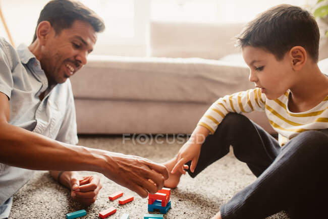 Vista lateral de pai e filho brincando com peças de construção na sala de jantar da casa — Fotografia de Stock