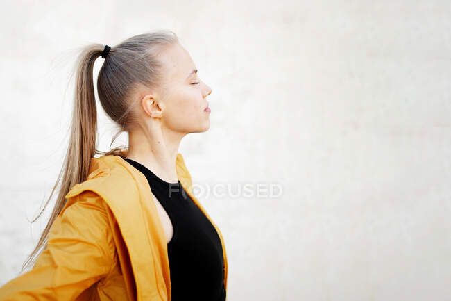 Seitenansicht einer jungen athletischen kaukasischen Frau, die sich draußen vor einer weißen Wand ausstreckt — Stockfoto
