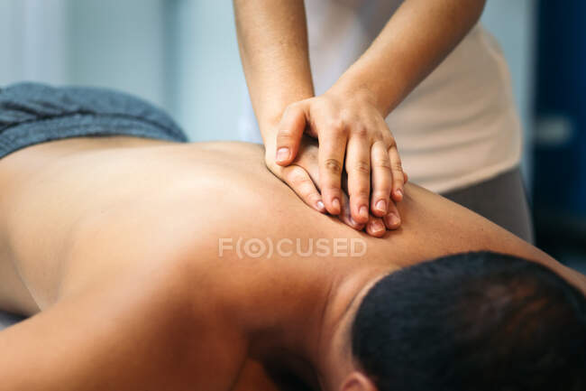 Розбита нерозпізнана жінка лікує чоловічого пацієнта фізіотерапією на спині. — стокове фото