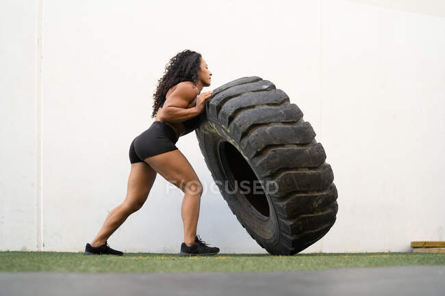 Seitenansicht einer muskulösen asiatischen Athletin, die während des intensiven Trainings schwere Reifen umkippt — Stockfoto