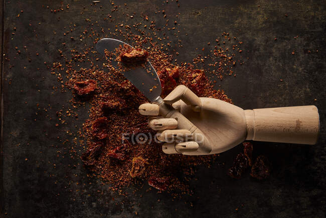 Zusammensetzung von oben mit verschütteten aromatischen natürlichen gemahlenen sonnengetrockneten Tomaten auf dunklem Tisch mit Messer in künstlicher Holzhand — Stockfoto