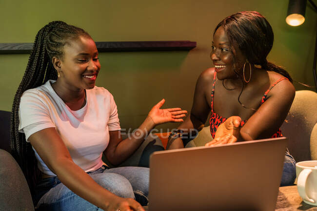 Cheerful African American female colleagues browsing laptop while working remotely in cafe and discussing business project — Stock Photo