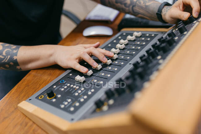 Crop unrecognizable sound man with tattoos adjusting faders on professional mixing console at table in music studio — Stock Photo