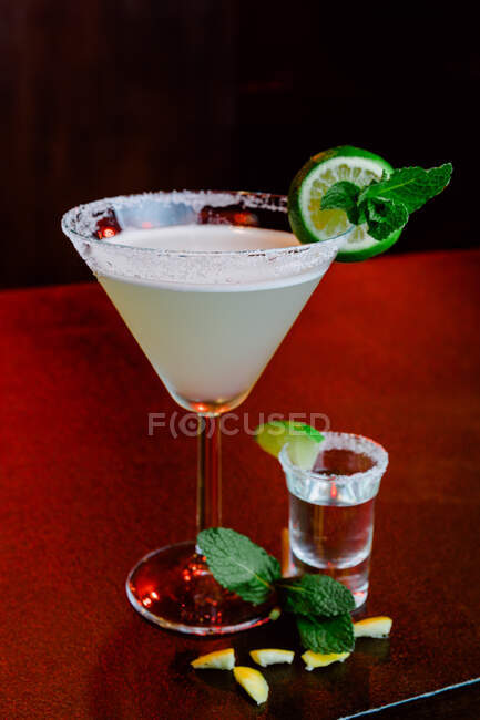 Kristallglas mit alkoholischem Cocktail Margarita bestehend aus Tequila-Orangenlikör und Limettensaft, serviert mit Salz am Glasrand und Minzblatt — Stockfoto