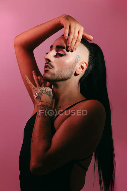 Vista laterale ritratto di glamour transgender donna barbuta in sofisticato make up in posa con gli occhi chiusi contro sfondo rosa in studio — Foto stock