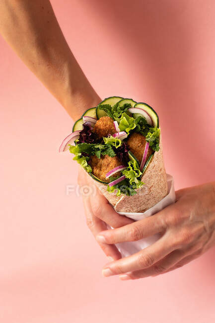 Cropped unrecognizable person hands holding vegan falafel wrap on colorful pink background — Stock Photo