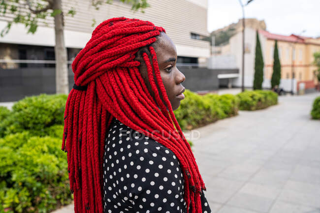 Vue latérale de la femme afro-américaine avec coiffure tressée debout dans le parc de la ville et regardant loin avec expression triste — Photo de stock