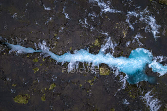 Сверху беспилотник видит мост, пересекающий бурный поток с голубой водой в пересеченной местности Исландии — стоковое фото