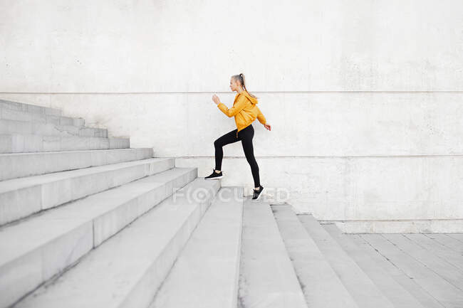Young athletic caucasian woman wearing headphones and sport outfit, running on stairs outdoors — Stock Photo