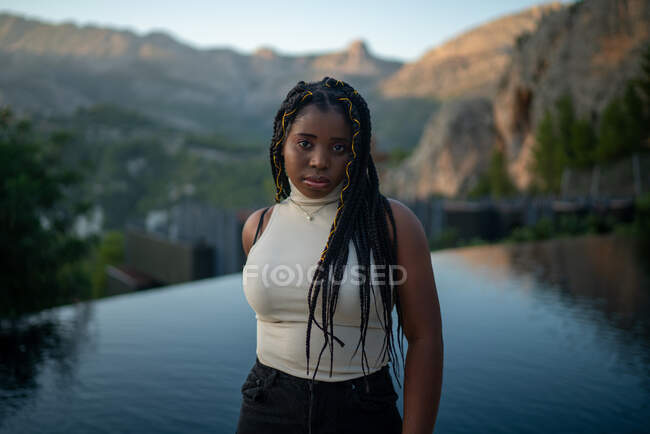Donna afroamericana con acconciatura intrecciata in piedi contro la piscina situata nel resort in altopiani — Foto stock
