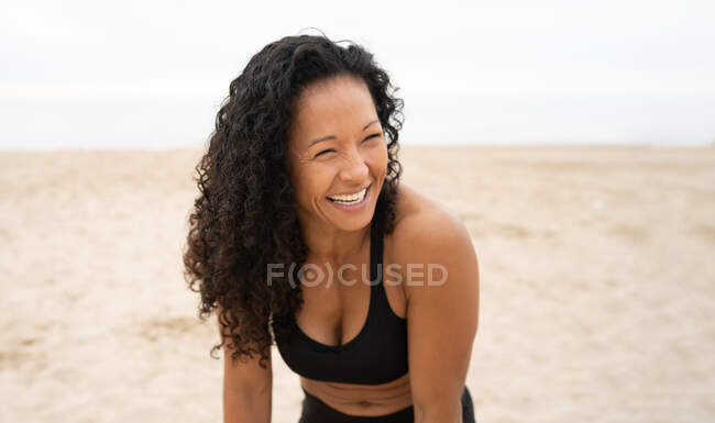Atleta feminina asiática positiva com cabelo encaracolado rindo na praia de areia no verão — Fotografia de Stock