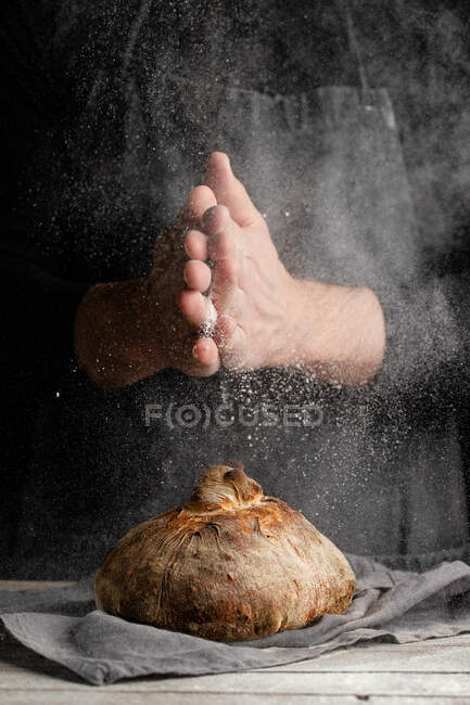 Unrecognizable chef in grembiule in piedi a tavola e decorare pagnotta di pane tradizionale con farina — Foto stock