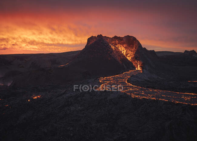Pintoresca vista del volcán activo con lava caliente situado contra el cielo nublado al atardecer en Islandia - foto de stock