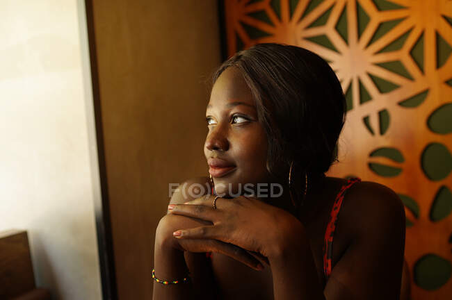 Peaceful African American female with braided hairstyle leaning on hands while enjoying weekend in cafe and looking away — Stock Photo