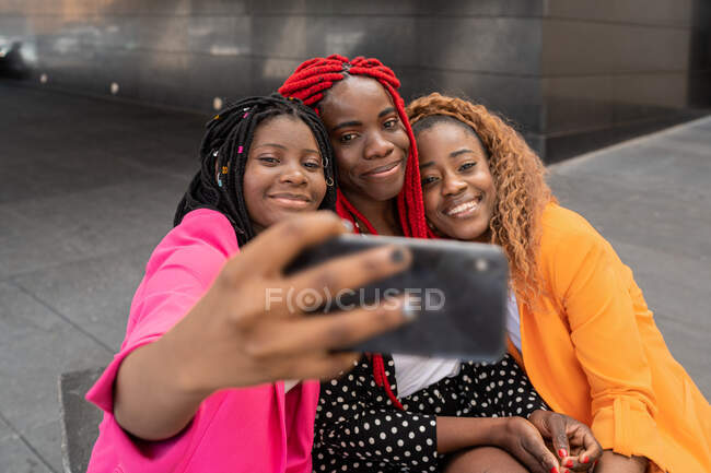 Афроамериканські найкращі друзі, які сидять поруч і фотографують на мобільному телефоні. — стокове фото