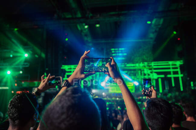 Retour personnes anonymes levant les bras avec des smartphones et enregistrant des performances musicales en direct sur la scène de la salle de concert — Photo de stock
