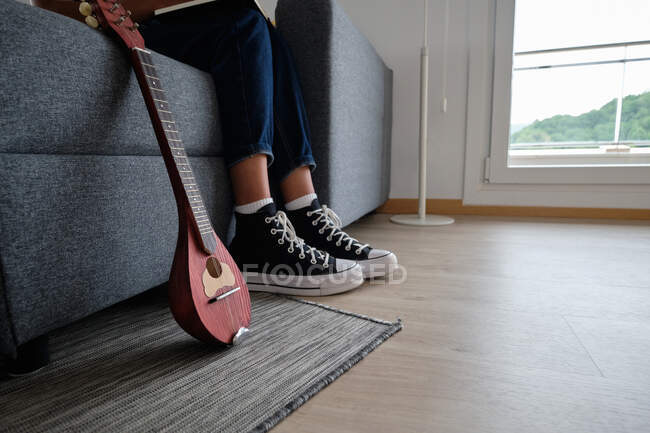 Cultivo irreconocible afroamericana mujer músico sentado en sofá cerca de mandolina - foto de stock
