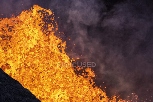Des éclaboussures de lave orange chaude surgissent du sommet volcanique entouré de fumée en Islande — Photo de stock