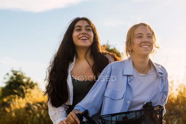 Deux jeunes femmes sur un vélo dans un champ au coucher du soleil — Photo de stock