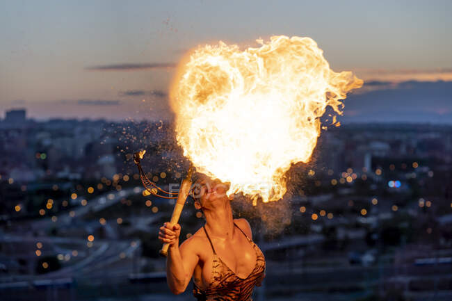Femme mangeuse de feu qui crache du feu au coucher du soleil — Photo de stock