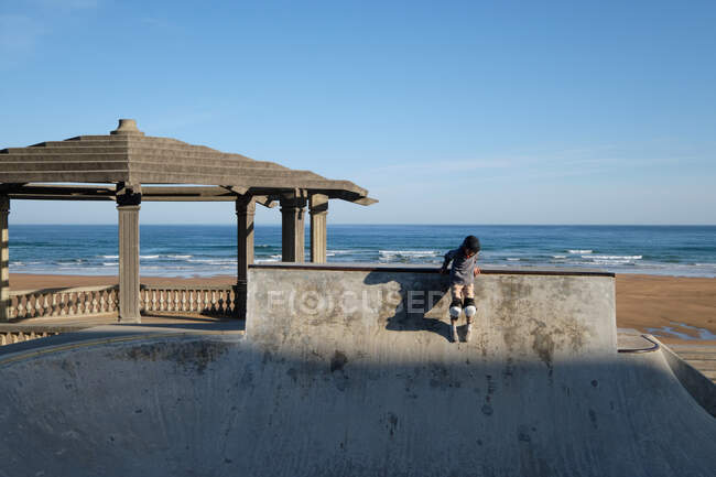 Unrecognizable teen boy in protective helmet riding skateboard in skate park on sunny day on seashore — Stock Photo