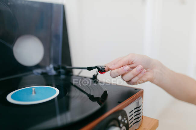 Side view of crop anonymous female turning on retro record player on shelf in house — Stock Photo