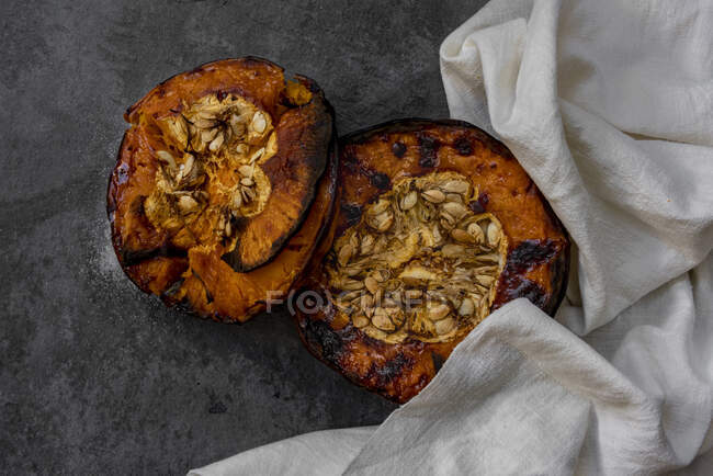 Dall'alto di metà di zucca al forno sane appetitose saporite con semi su tavolo grigio con stoffa da cucina — Foto stock