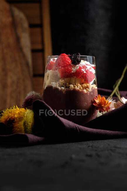 Ciotola di frullato appetitosa con fragole di muesli e mirtilli messi in tavola vicino a vari fiori selvatici — Foto stock