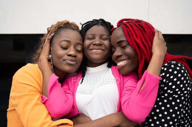 Alegre afro-americano feminino melhores amigos sorrindo alegremente e abraçando uns aos outros com os olhos fechados — Fotografia de Stock