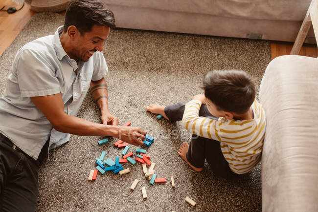Desde arriba padre e hijo jugando con piezas de construcción en el comedor de la casa - foto de stock