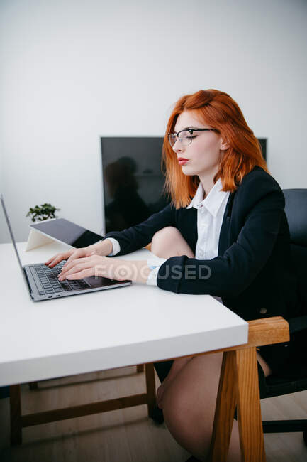 Vista laterale della giovane imprenditrice che lavora su netbook alla scrivania con tablet e smartphone a casa — Foto stock