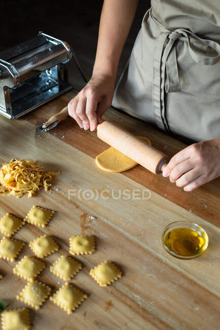 Pessoa irreconhecível preparando raviolis e massas em casa. Ela está usando um rolo de madeira — Fotografia de Stock